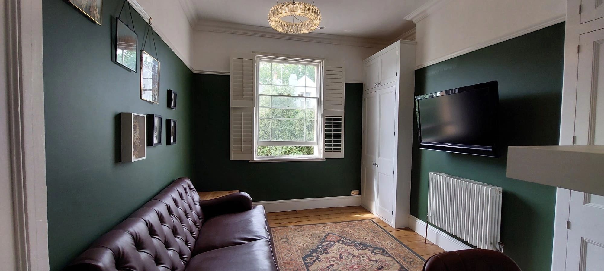 Dark green lounge wall with white sash window, leather sofa and built-in cupboard.