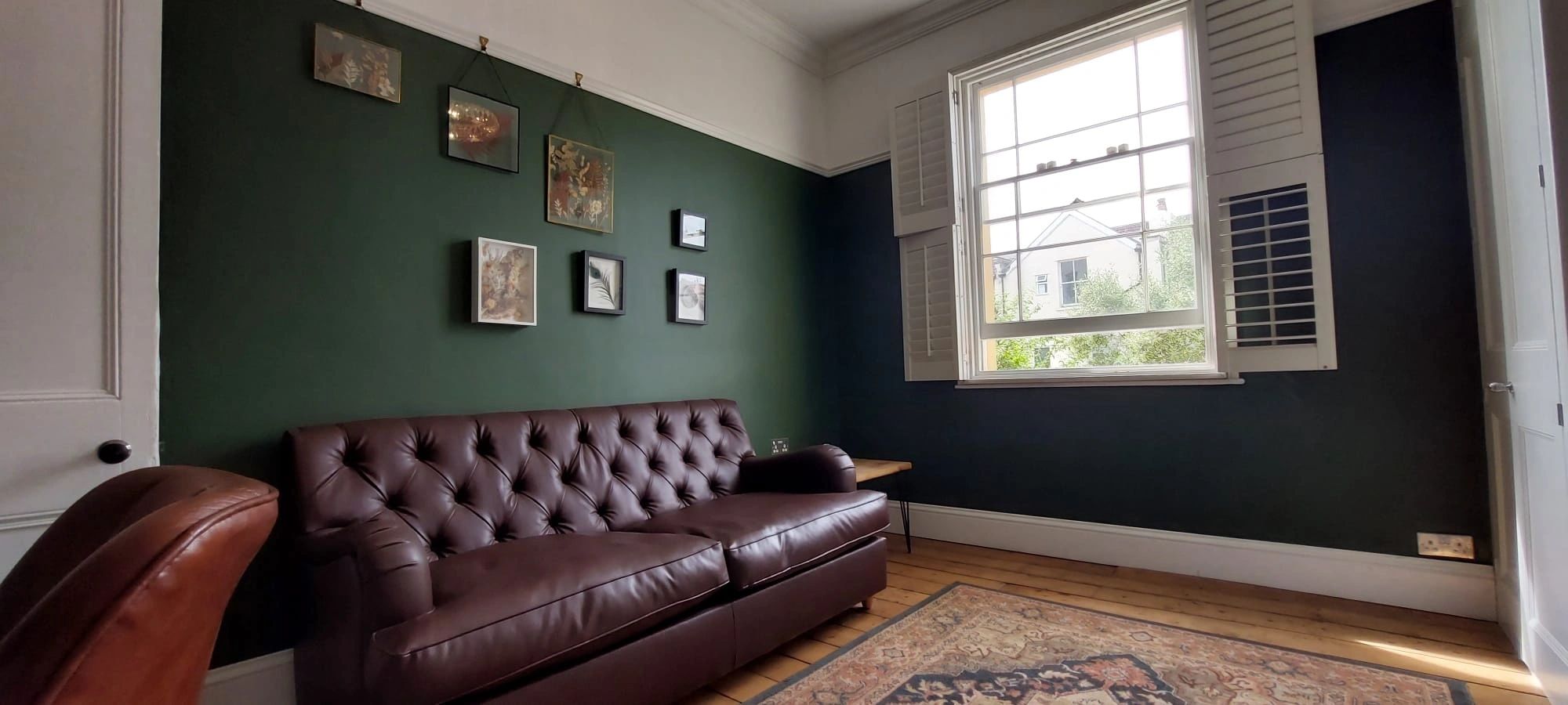 Dark green lounge angle showing sofa, shutters, wall art and period proportions.
