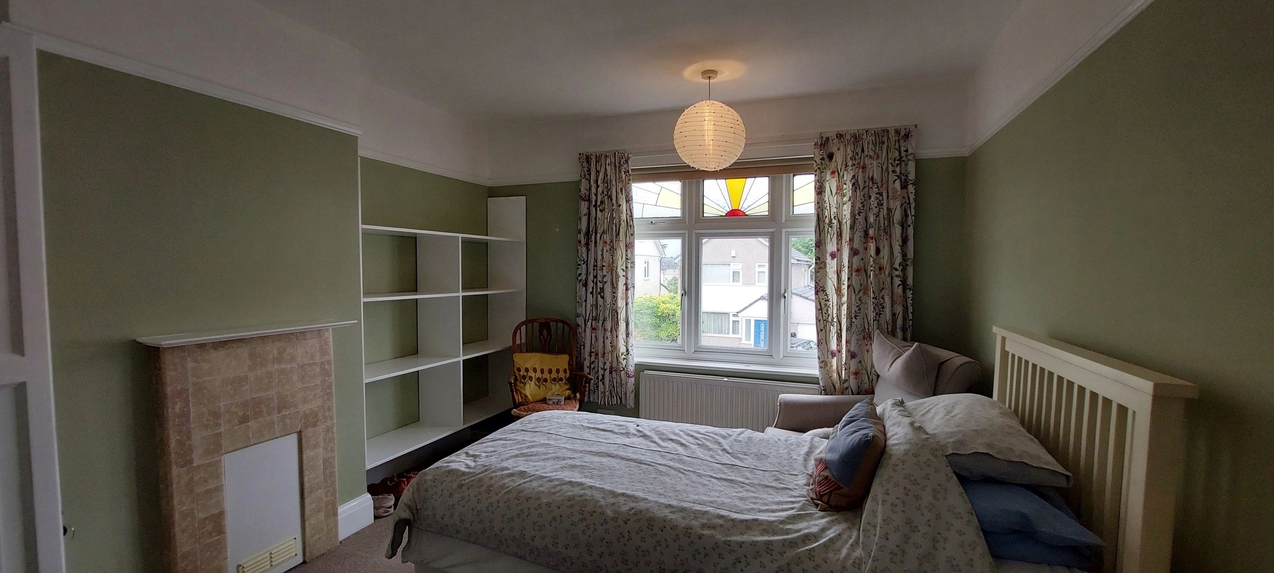 Bedroom with muted green walls, white trim and stained-glass upper window, decorated by Warrilow.
